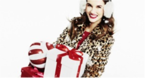 Smiling woman in earmuffs, cheetah-print jacket and red shirt holding a gift and large ornament