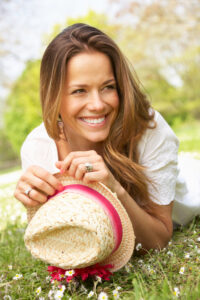 Woman lying on her stomach in the grass outdoors holding onto a straw hat