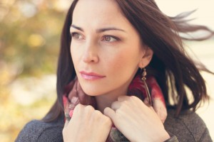Woman in a scarf and coat gazing intensely to the left with her hands holding onto her scarf