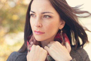 Woman in a scarf and coat gazing intensely to the left with her hands holding onto her scarf