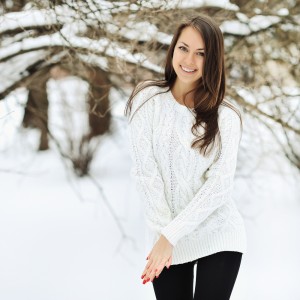 Smiling woman with long brown hair in the snow outdoors wearing a white knit sweater