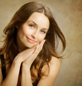 Woman with long brown flowing hair smiling and resting her head on the sides of her hands