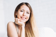 Woman with long brown hair smiling while resting her head on her hand