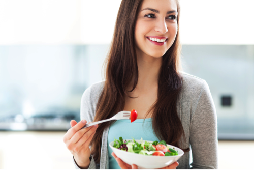 Woman with long brown hair smiling while eating a salad