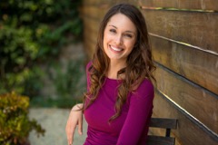 Woman with long brown hair sitting on a chair outdoors smiling