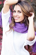 Woman in a white knit top and purple scarf smiling outdoors