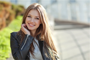 Young woman with long brown hair in a black leather jacket smiling outdoors