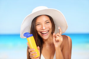 Joyful woman in a beach hat smiling while applying sunscreen to her nose