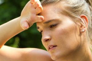 Tired-looking woman in the sun wiping sweat off her forehead