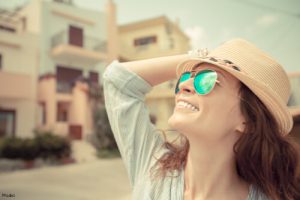 woman wearing a hat and sunglasses looking up and smiling