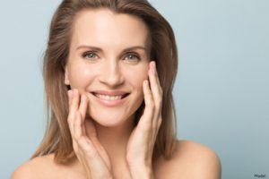 Mature woman smiling and gently touching her face with her hands