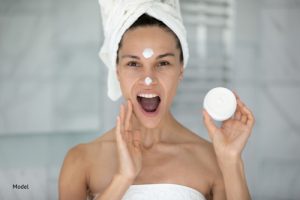 Woman with her mouth open applying skin care cream to her face