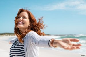 Joyful woman with red hair at the beach smiling with arms outstretched