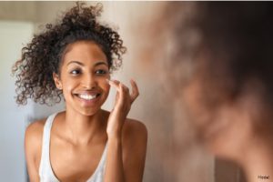 Happy, smiling woman applies skin care in the mirror
