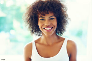 Woman in a white tank top smiling in front of a green background