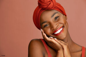 Woman in a red hair wrap smiling and resting her head in her hands