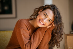 Joyful brunette woman smiling and resting her head on her hands