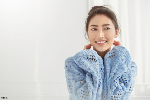 Young woman smiling in a blue knit sweater in front of a white background