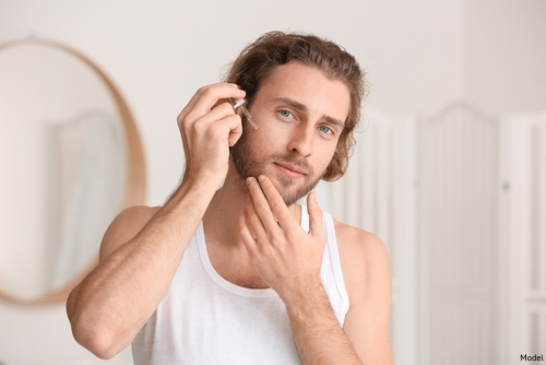 Brunette man applies skin care serum to his face