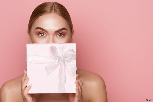 Woman wearing pink eyeshadow holding a light pink gift box in front of her face