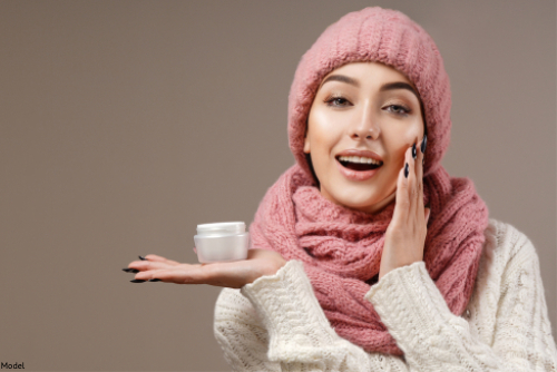 Woman in a knit hat, scarf and sweater applying skin care
