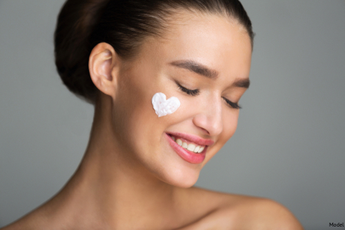 Smiling woman with skincare cream on her face in the shape of a heart
