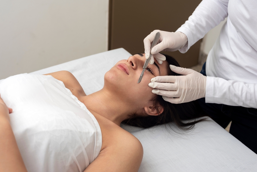 Young woman lying on a treatment table at a beauty center receiving a dermaplaning facial, a non-invasive skincare technique used to exfoliate dead skin cells and reveal smoother, glowing skin.