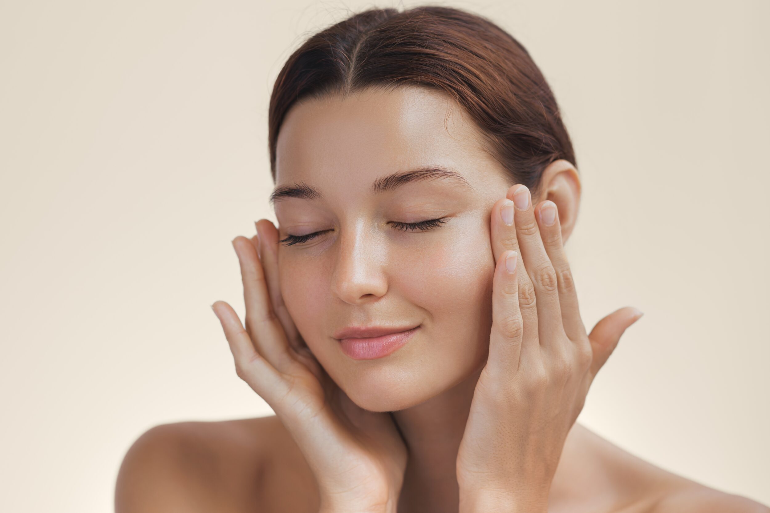 A woman with glowing, hydrated skin gently touches her face, enjoying the smooth results of a BBL photofacial skincare treatment