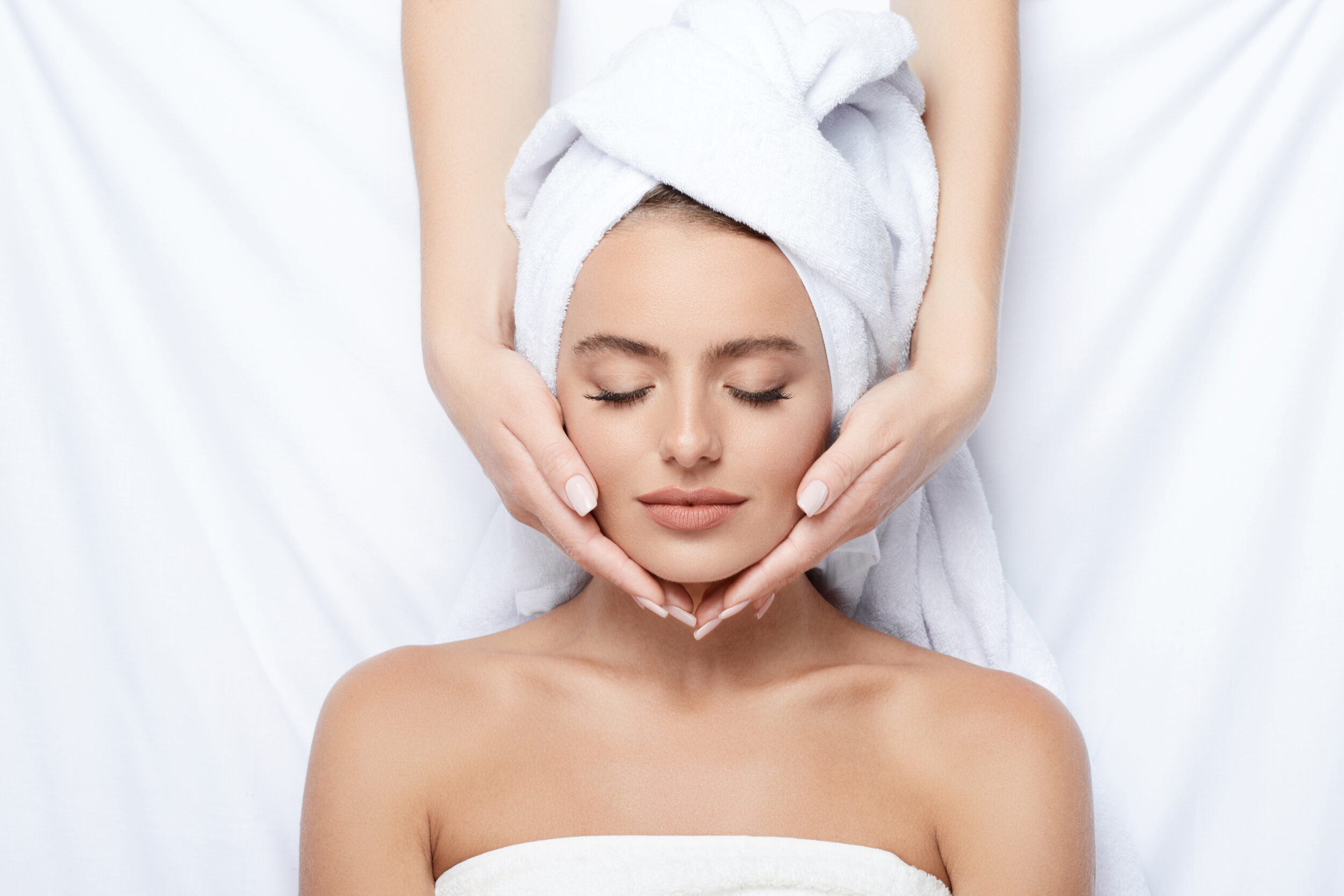 A young woman with flawless skin and thick eyebrows relaxes with a towel on her head after a BBL photofacial and spa skincare treatment