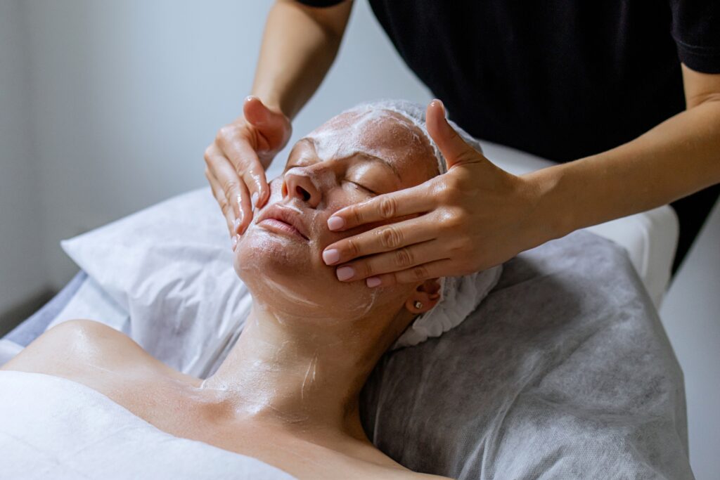 Woman receiving facial massage in beauty salon, anti-aging skincare treatment with cosmetology specialist performing lifting massage in spa