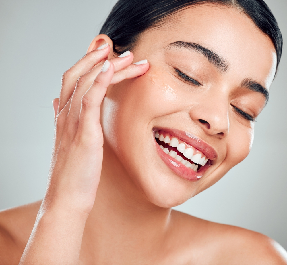 Smiling woman applying serum in studio, concept of beauty, skincare, collagen boost, and vitamin C self-care for glowing skin.